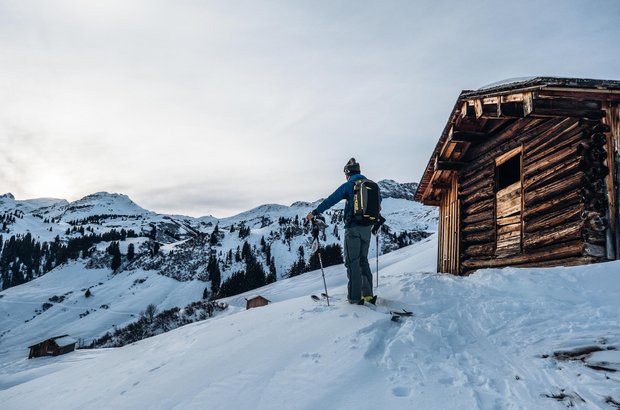Hütte in Lech Skitourengeher steht neben einer urigen Hütte und genießt den Ausblick auf die Berge