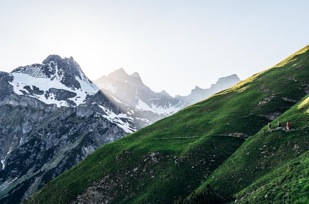 Lech Wanderung Drei Personen wandern an einem schmalen Pfad entlang mit Ausblick auf die schroffen Gipfel.